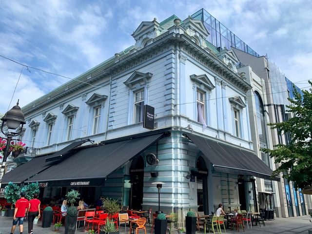 A pale blue neo-Renaissance corner building on Knez Mihailova, with a café terrace below