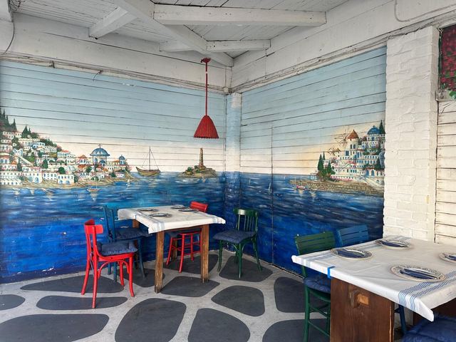 Painted harbour murals and red and green chairs in the dining room at Me Agapi