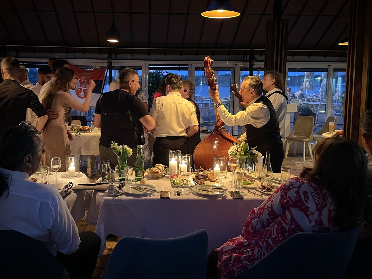 Musicians play between candlelit tables at a riverside restaurant on the Zemun Quay at dusk